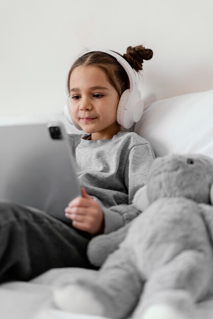 Маленькая девочка в постели с наушниками с помощью планшета