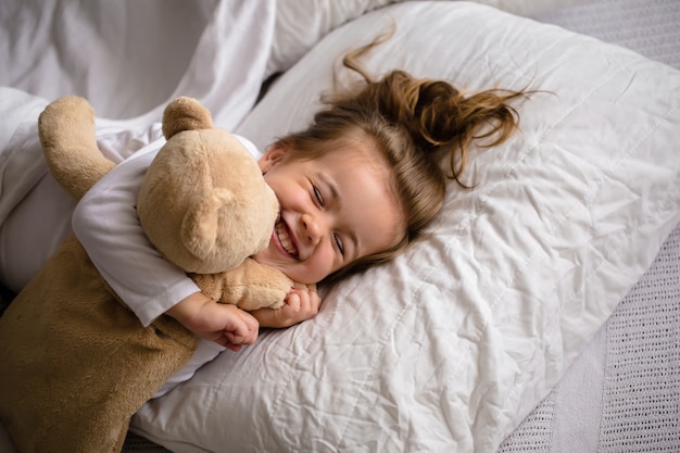 柔らかいおもちゃが付いているベッドの小さな女の子は子供の感情