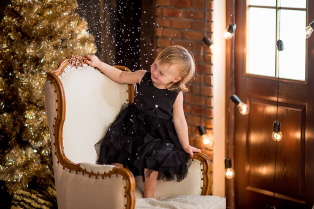 Little girl in black dress sits among Christmas decorations