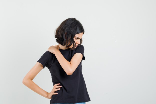 Little girl in black t-shirt having neck pain and looking uncomfortable , front view.