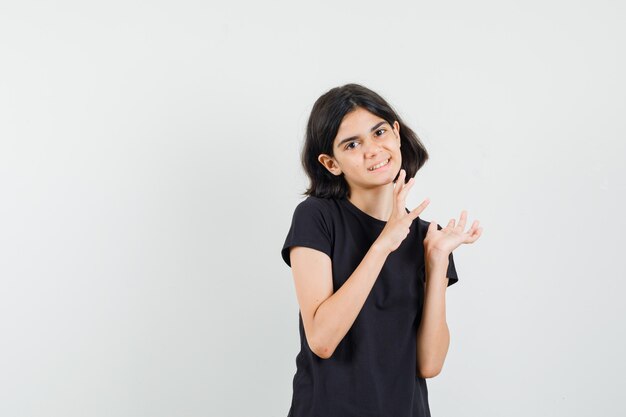 Little girl in black t-shirt keeping hands as grabbing something and looking cheery , front view.