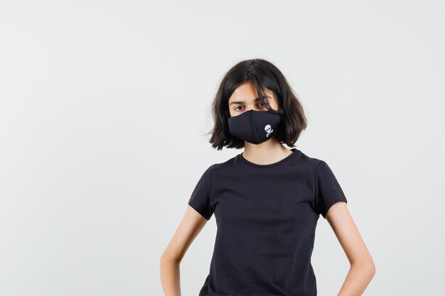 黒のTシャツを着た少女、腰に手をつないで自信を持って見えるマスク、正面図。