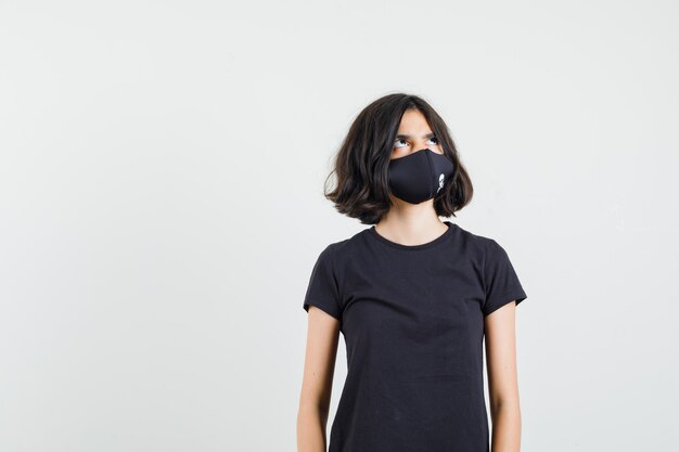 黒のTシャツを着た少女、見上げて物思いにふけるマスク、正面図。