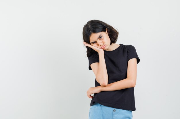 Little girl in black t-shirt, shorts having painful toothache and looking unwell , front view.