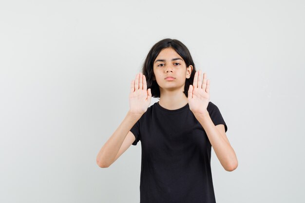 Little girl in black t-shirt showing stop gesture and looking annoyed , front view.