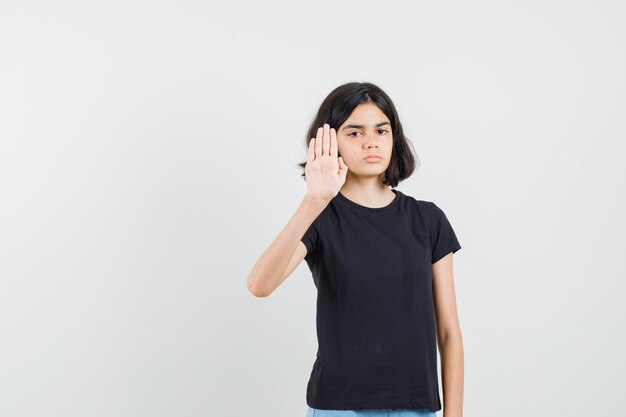 Little girl in black t-shirt showing stop gesture and looking serious , front view.