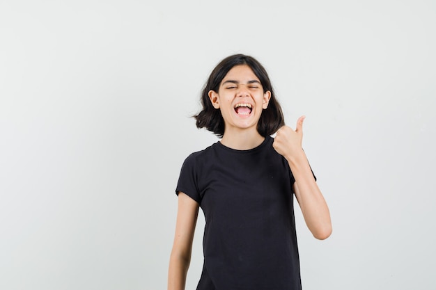 Little girl in black t-shirt showing thumb up and looking happy , front view.