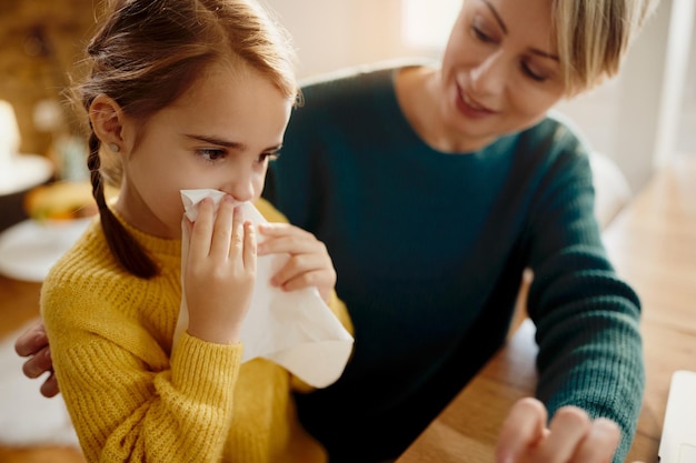 Little girl blowing nose while being with her mother at home