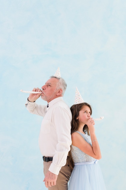 お祝いの時に彼女の祖父とパーティーの送風機を吹く少女