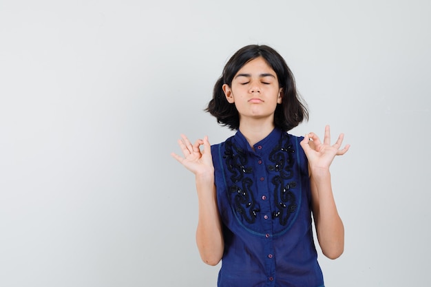 Little girl in blue blouse doing meditation with closed eyes and looking relaxed , front view.