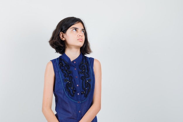 Little girl in blue blouse looking up and looking thoughtful.