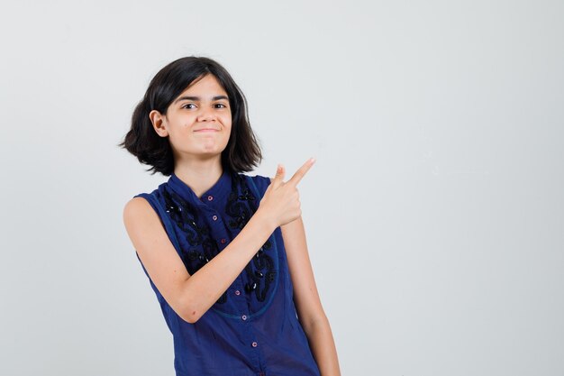 Little girl in blue blouse pointing at upper right corner and looking glad