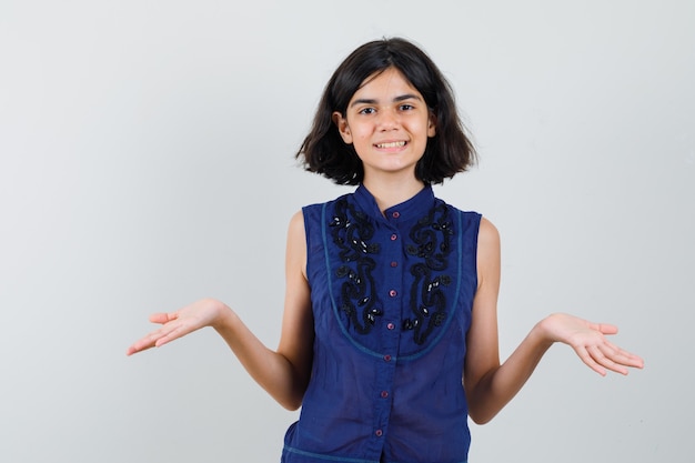 Little girl in blue blouse pretending to show something and looking glad