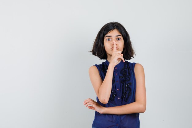 Little girl in blue blouse showing silence gesture and looking careful