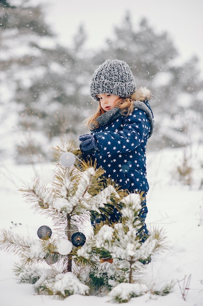 Little girl in a blue hat playing in a winter forest