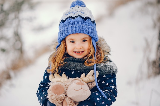 Bambina in un cappello blu che gioca in una foresta di inverno