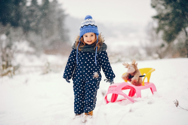 Little girl in a blue hat playing in a winter forest