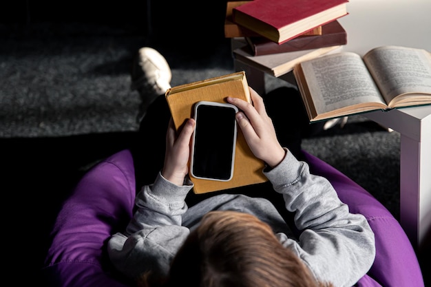 Little girl among the books uses a smartphone