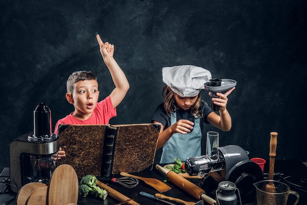 Little girl and boy are cooking vegetables and reading old recipe book.