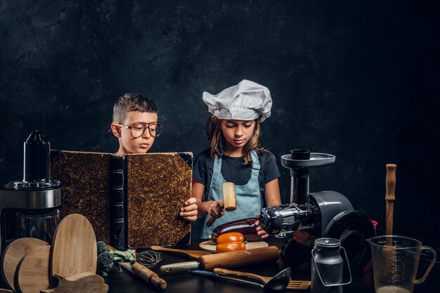 Little girl and boy are cooking vegetables and reading old recipe book.