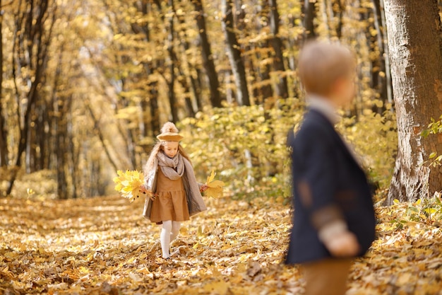 Bambina e ragazzo nella sosta di autunno. ragazza che tiene foglie gialle e cammina. il ragazzo è sfocato sulla foto.