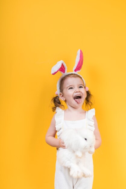 Little girl in bunny ears with rabbit showing tongue