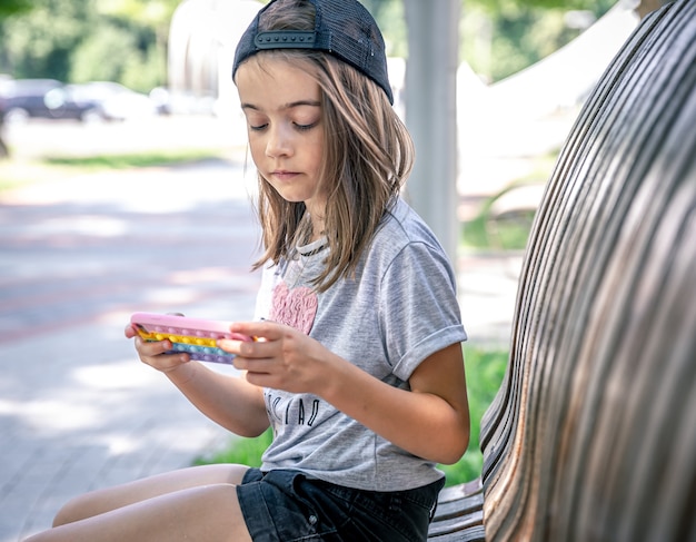 帽子をかぶった少女は、夏の日に公園のベンチに座っているスマートフォンを使用しています。