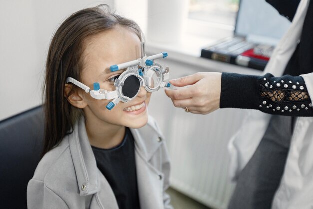 Little girl checking up her sight at ophthalmology center. Female optometrist doing sight testing. Brunette girl wearing grey jacket and black shirt.