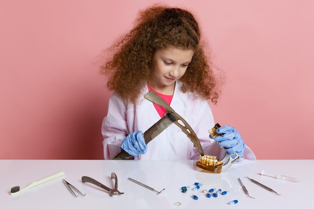 Free photo little girl, child in image of dentist working with fake teeth isolated on pink background