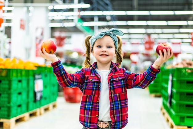 Маленькая девочка, выбирая яблоко в продуктовом магазине или супермаркете