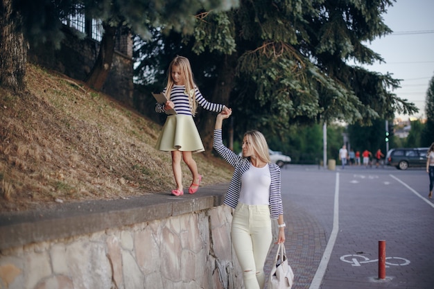 Little girl climbing a stone wall while grabbing her mother's hand