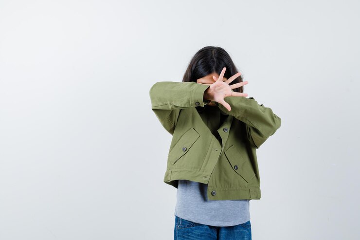 免費 Photo 小女孩穿着外套,t恤,牛仔裤用手遮住眼睛, 露出手掌, 看起来害怕, 前景.