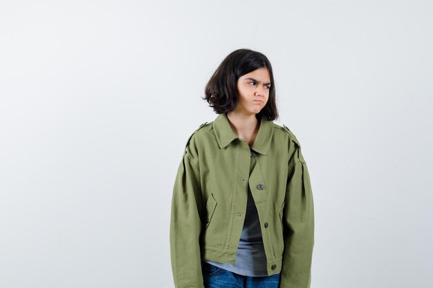 Little girl in coat, t-shirt, jeans looking away and looking wistful , front view.