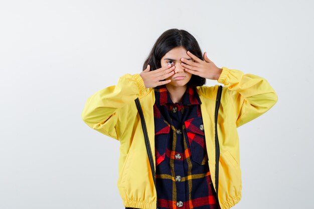 Little girl covering eye with hand in checked shirt, jacket and looking serious 