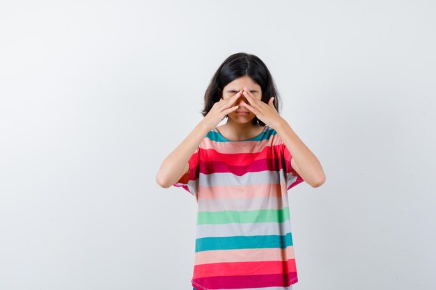 Little girl covering eyes with hands in t-shirt and looking sleepy. front view.