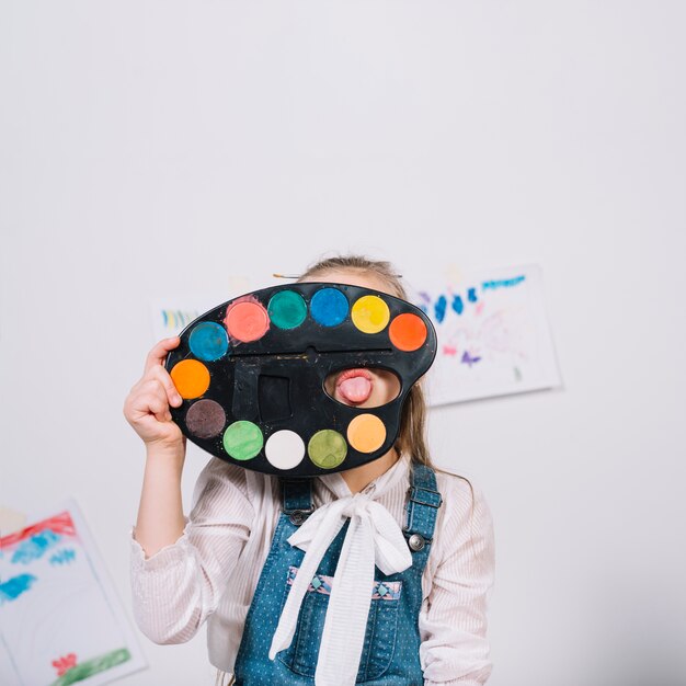 Little girl covering face with palette and showing tongue 