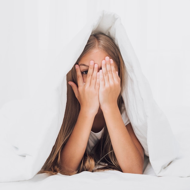 Free photo little girl covering her eyes under blanket