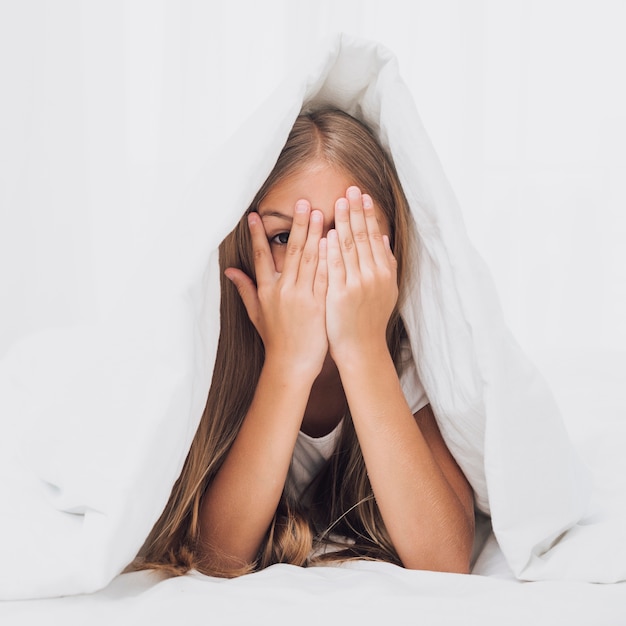 Little girl covering her eyes under blanket 