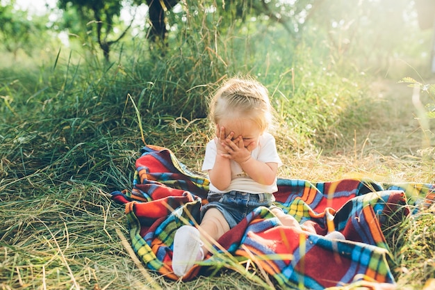 Bambina che copre il viso, seduta su una coperta sul pavimento