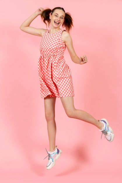 little girl in cute bright dress jumping on pink