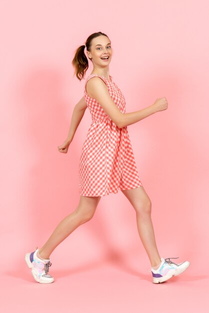 маленькая девочка в милом ярком платье счастливо позирует на розовом