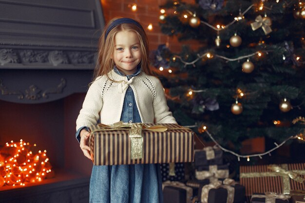 Little girl in a cute dress near christmas tree with present