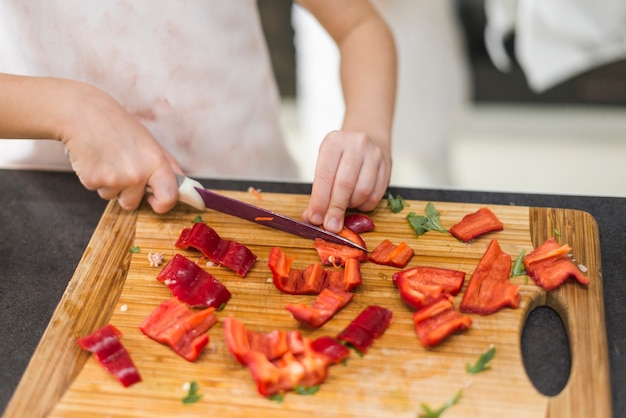 Little girl cutting red bell pepper on chopping board