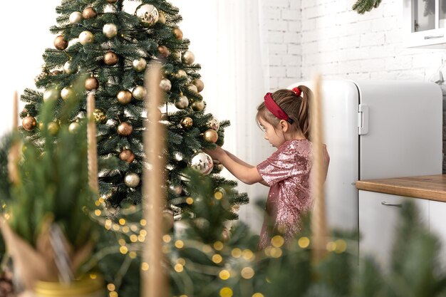 A little girl decorates a christmas tree hangs balls
