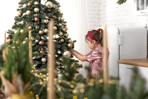 A little girl decorates a christmas tree hangs balls