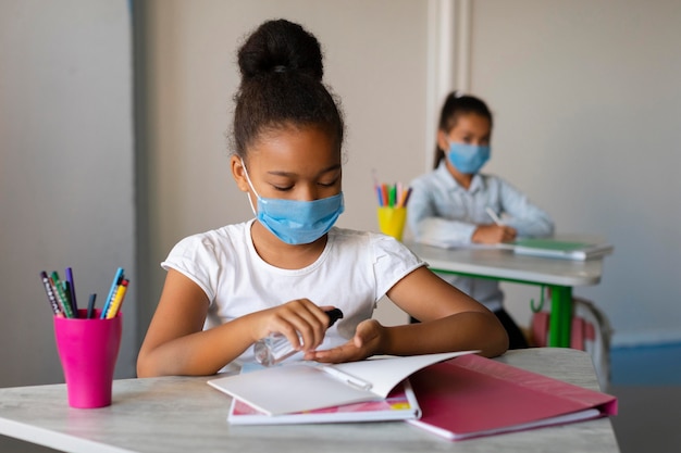 Free photo little girl disinfecting her hands in class