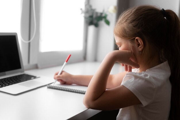 Little girl doing homework at home with laptop and notebook