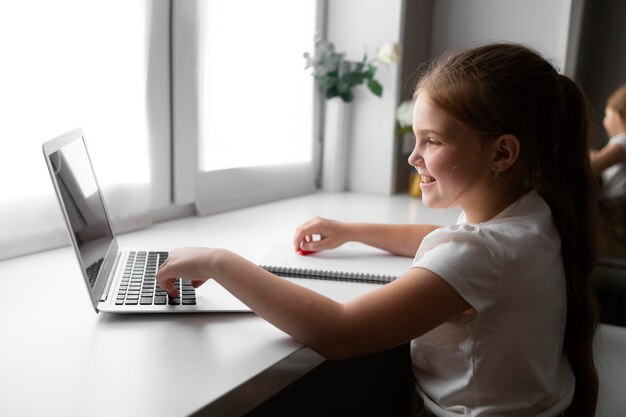 Little girl doing homework at home with laptop and notebook