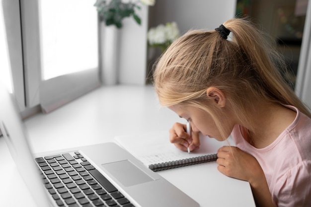 Free photo little girl doing homework at home with laptop and notebook