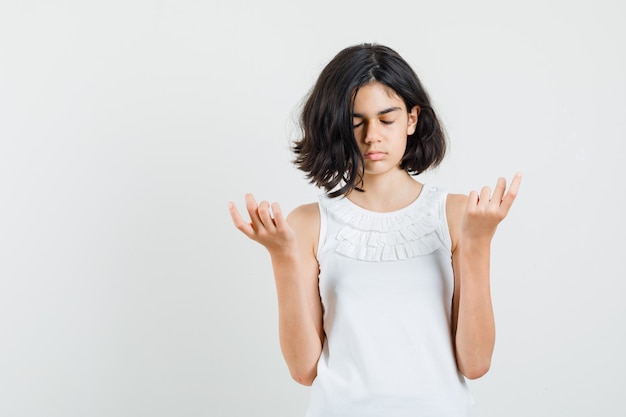 Little girl doing meditation with closed eyes in white blouse and looking calm. front view.